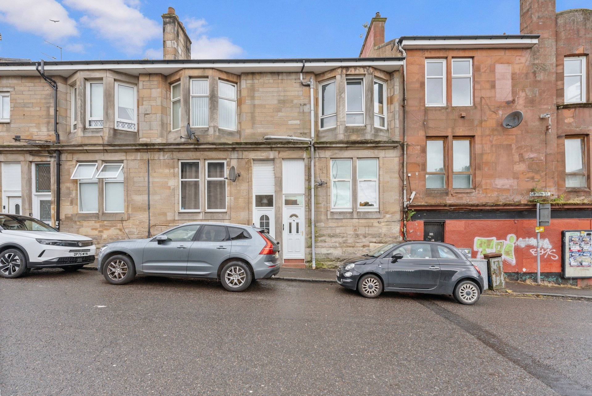 Stone terraced house exterior with parked cars on street and neighbouring properties