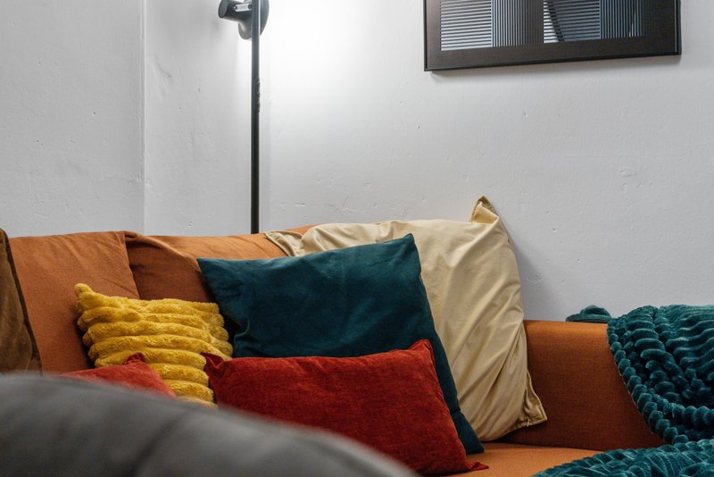Orange sofa with colorful cushions and throws in living room with white walls