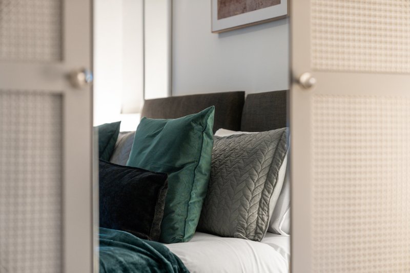 Bedroom with double bed, green and gray cushions, headboard, and mirror reflection