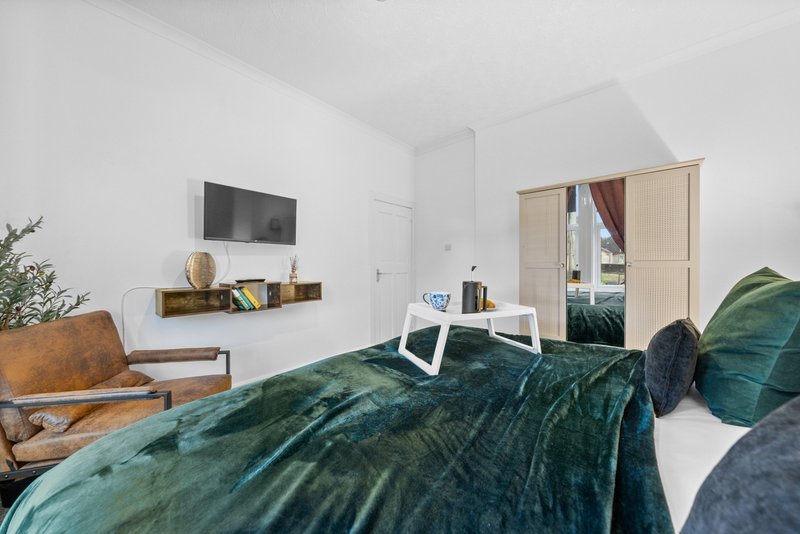 Modern bedroom with teal bedding, wooden furniture, wall-mounted shelf and desk area