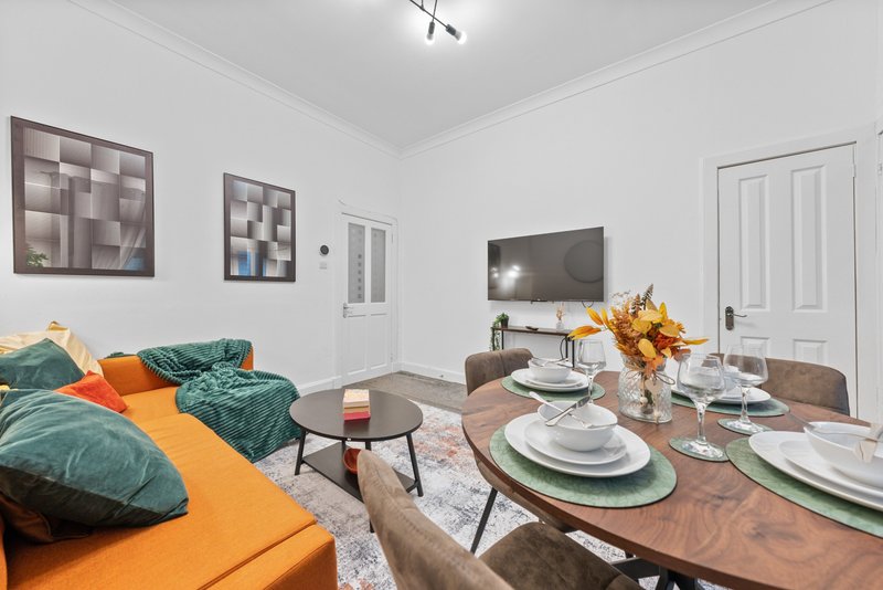 Open-plan living and dining area with sofa, dining table, TV, and kitchen in background