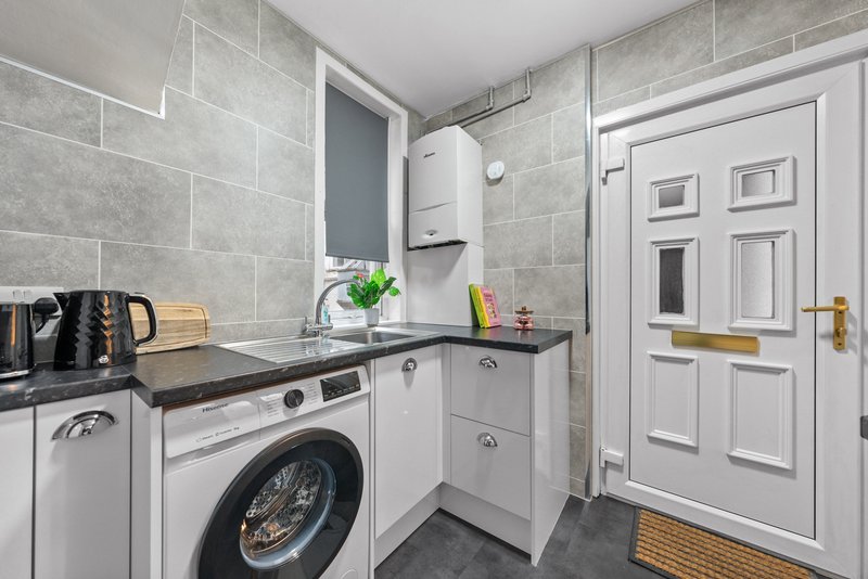 Modern utility room with washing machine, white cabinetry, grey tile walls and white door