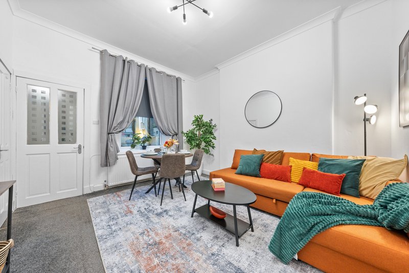 Modern living room with orange sofa, colorful cushions, dining area and potted plant