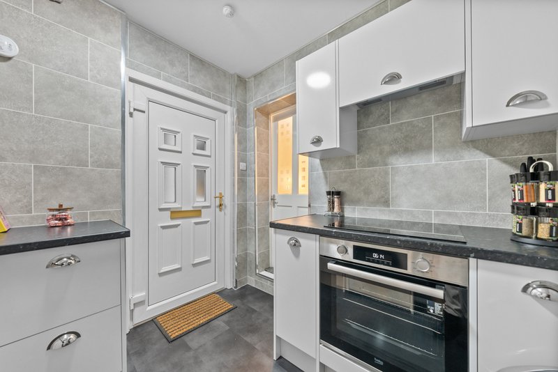Modern kitchen with white cabinetry, gray tile splashback, built-in oven and door to hallway