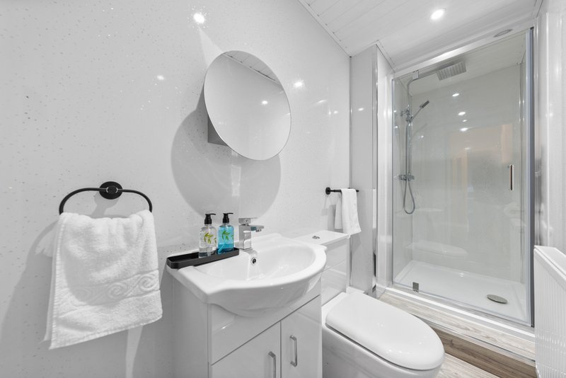 Modern bathroom with white vanity, round mirror, toilet, and glass shower enclosure