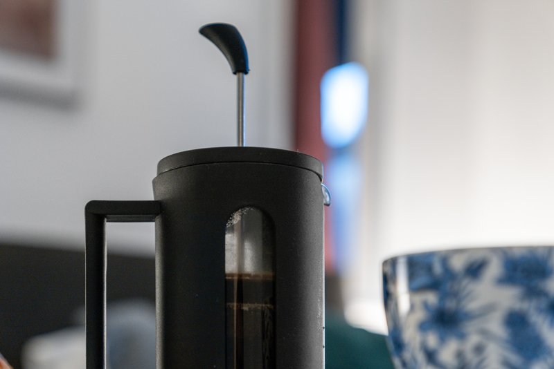 Black coffee press with plunger on kitchen counter, blurred background