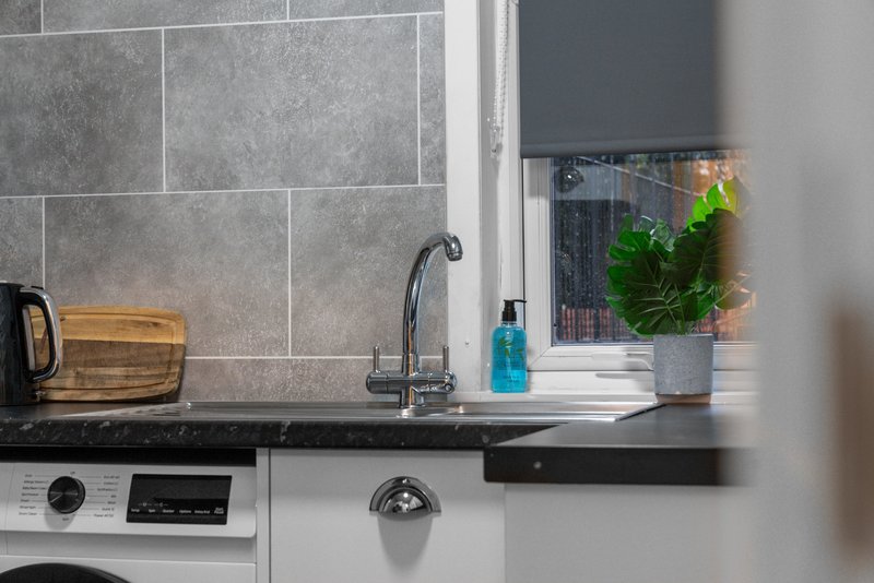 Modern kitchen with gray tile backsplash, black countertop, sink, faucet and potted plant