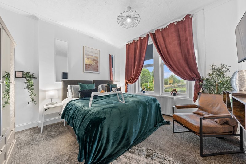 Bright bedroom with teal bed, burgundy curtains, wooden chair, plants and window view