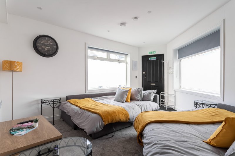Modern twin bedroom with yellow bedding, large windows, wall clock and wooden side table