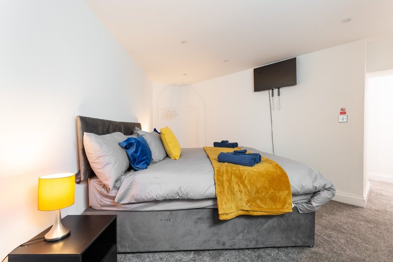 Modern bedroom with gray bed, yellow lamp, colorful pillows and throws, mounted TV