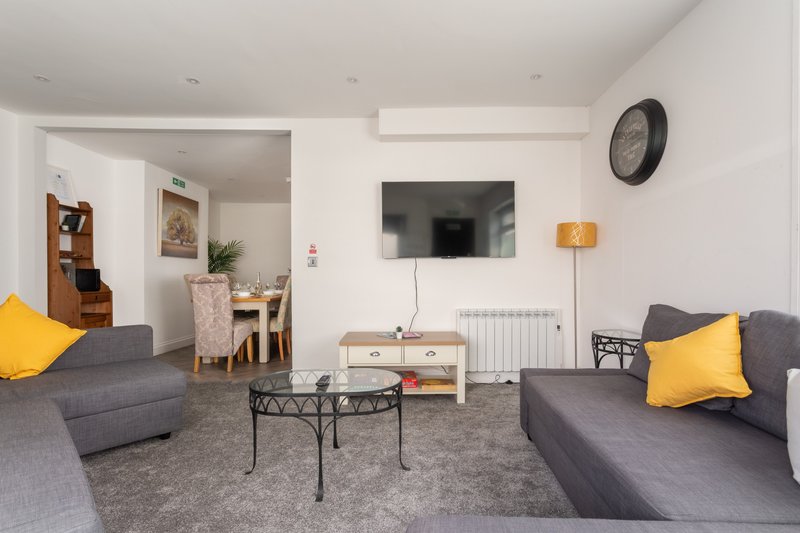 Open-plan living room with grey sofas, yellow cushions, TV, dining area and kitchen visible
