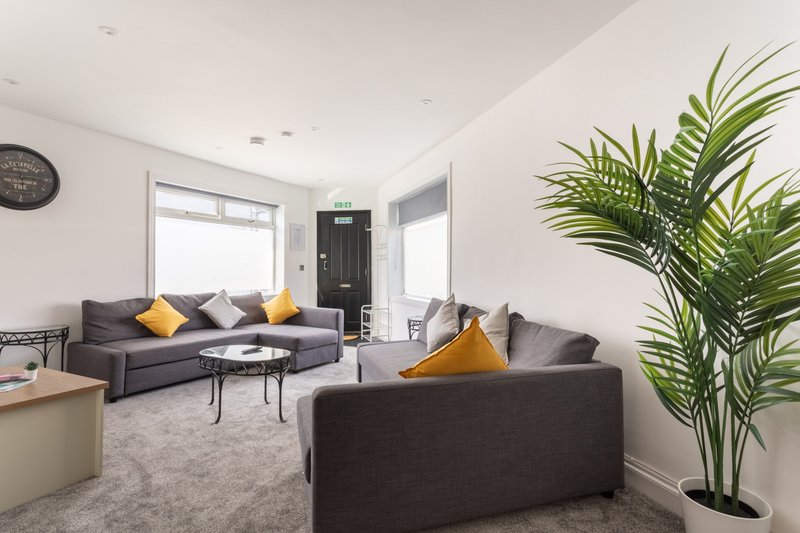Modern living room with grey sofas, yellow cushions, potted plant and wall clock