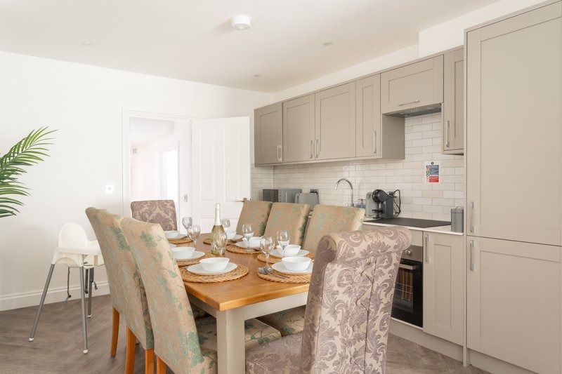 Open-plan kitchen and dining area with wooden table, upholstered chairs, and fitted cabinetry