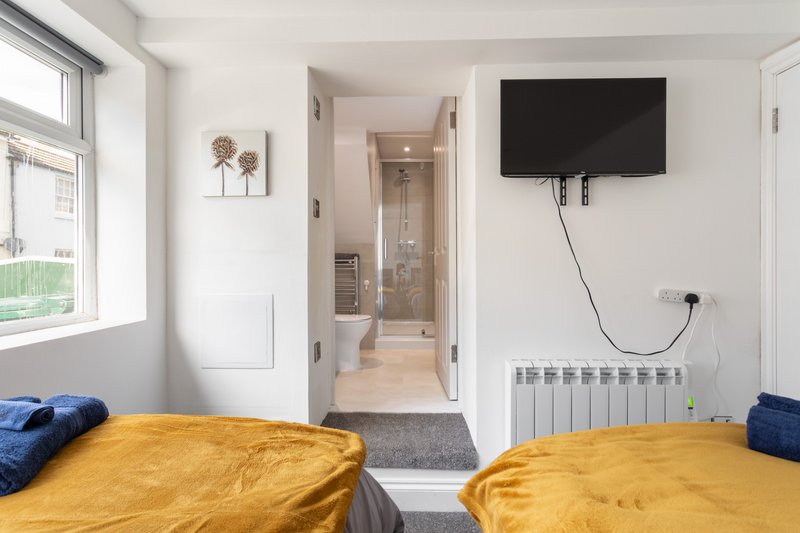 Bright bedroom with two beds with yellow duvets, wall-mounted TV, and ensuite bathroom