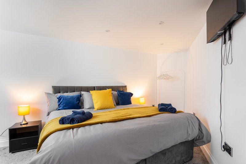 Modern bedroom with double bed, yellow and blue bedding, grey headboard, and bedside lamps