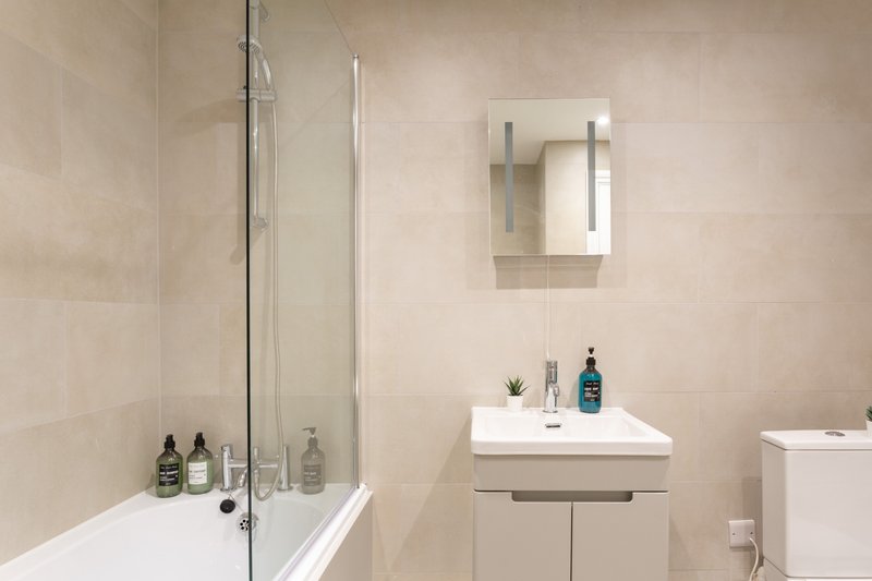 Modern bathroom with bathtub, shower screen, vanity sink, mirror and toiletries
