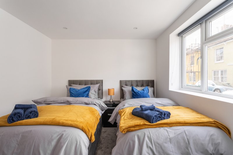 Twin bedroom with yellow bedding, blue pillows, grey headboards and large window