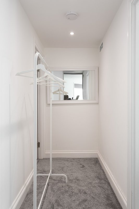 Narrow utility room with white clothes rail, gray carpet, and pass-through window
