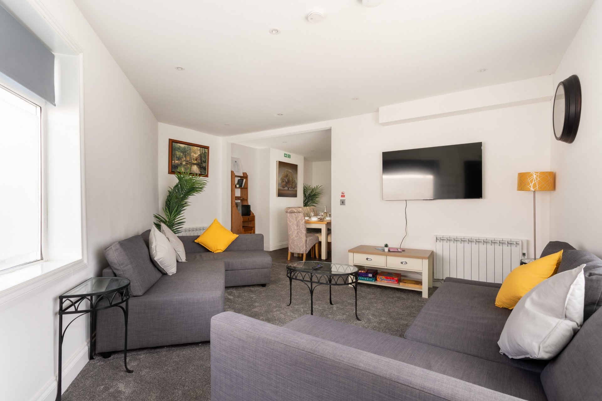 Modern living room with grey sofas, yellow cushions, TV, plants and natural light