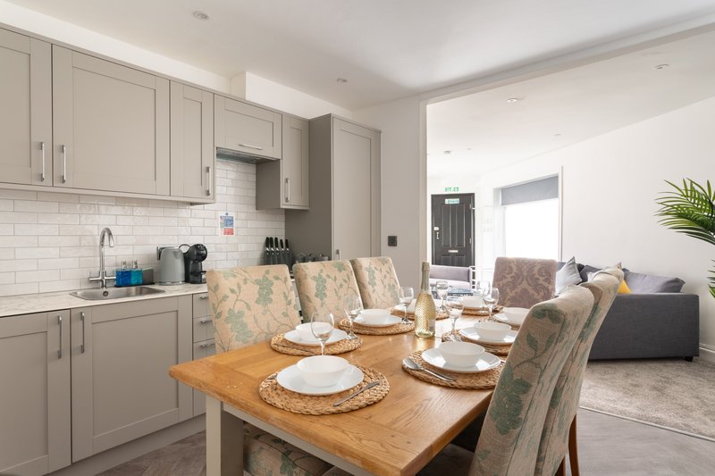 Open-plan kitchen and dining area with wooden table, upholstered chairs, and cream cabinetry