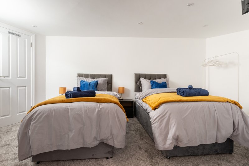 Bright bedroom with two single beds, gray bedding, blue and yellow accents, wooden headboards