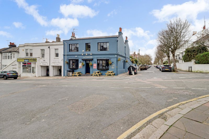 Street view of blue corner building with shop fronts and residential properties