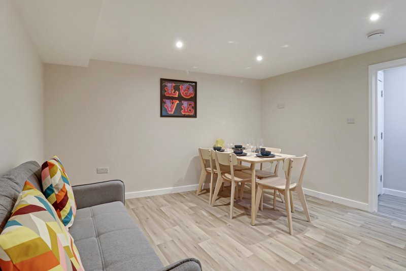 Open-plan living and dining area with gray sofa, wooden dining table, chairs, and wall art