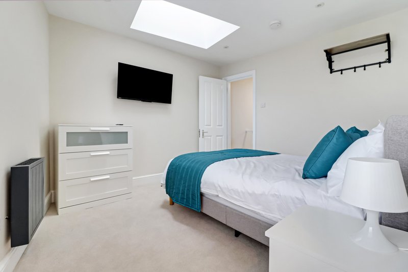 Bright modern bedroom with double bed, blue bedding, wall-mounted TV and white furnishings