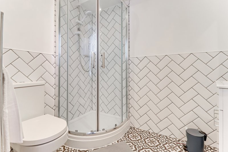 Modern bathroom with curved glass shower enclosure, herringbone tile pattern, and toilet