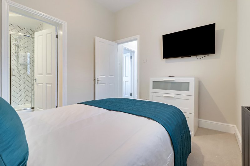 Modern bedroom with double bed, wall-mounted TV, ensuite bathroom and white furnishings