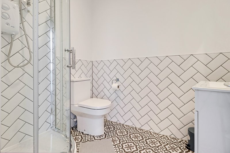 Modern bathroom with herringbone tile walls, walk-in shower, toilet and patterned floor