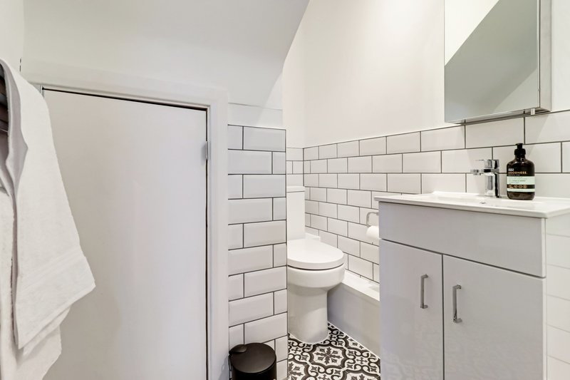 Modern bathroom with white subway tile, toilet, vanity with mirror, and patterned floor