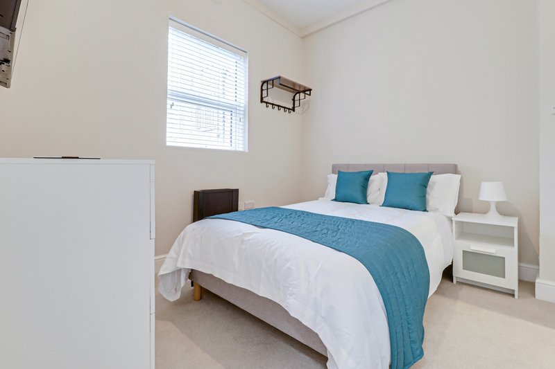Bright bedroom with double bed, blue bedding, white nightstands and window with blinds