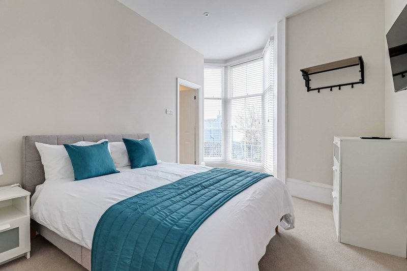 Modern bedroom with double bed, teal bedding, white pillows and bright windows