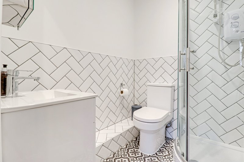 Modern bathroom with herringbone tile walls, white vanity, toilet, and walk-in shower