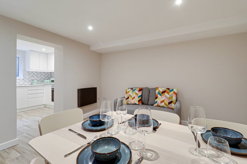 Modern dining area with white table, place settings, and sofa with patterned cushions in background