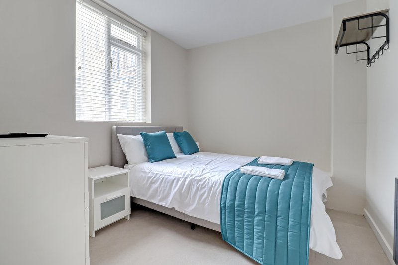 Bedroom with single bed, teal bedding, white nightstand, and window with blinds
