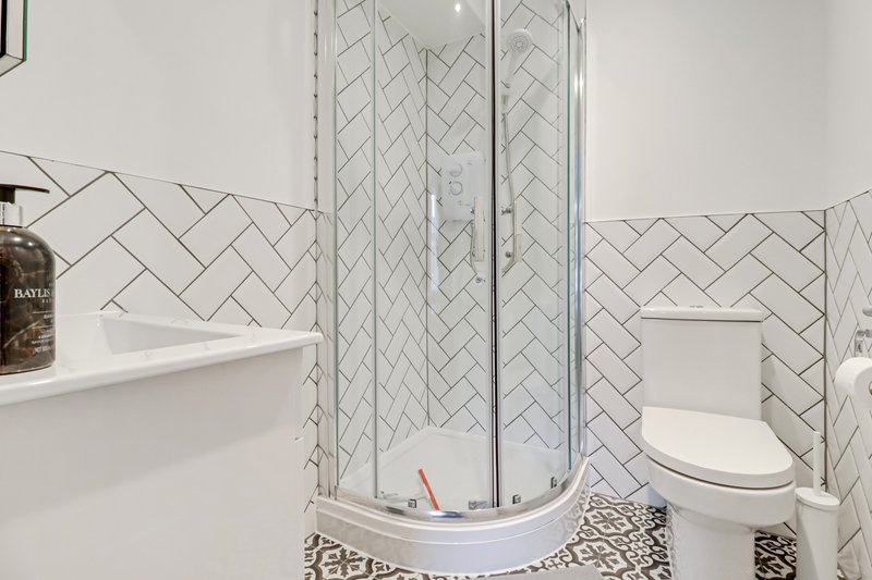 Modern bathroom with herringbone tile shower enclosure, toilet, and white sink vanity