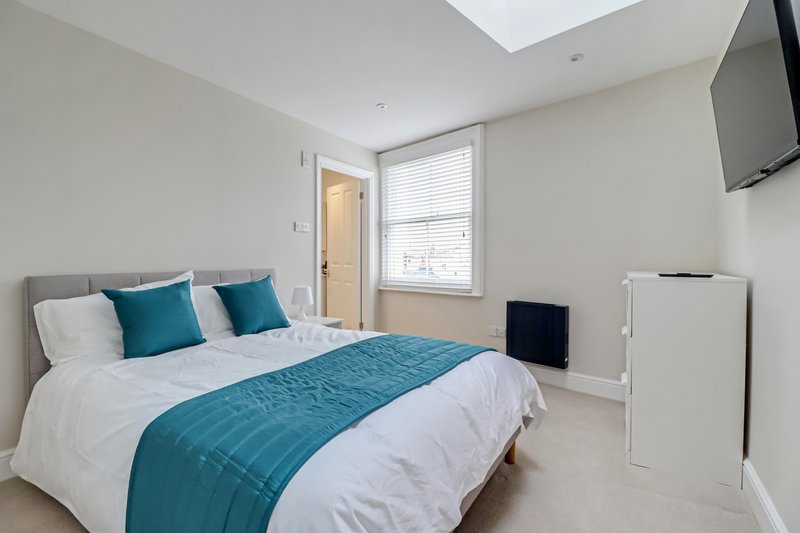 Bright bedroom with double bed, teal bedding, white pillows, window and wall-mounted TV