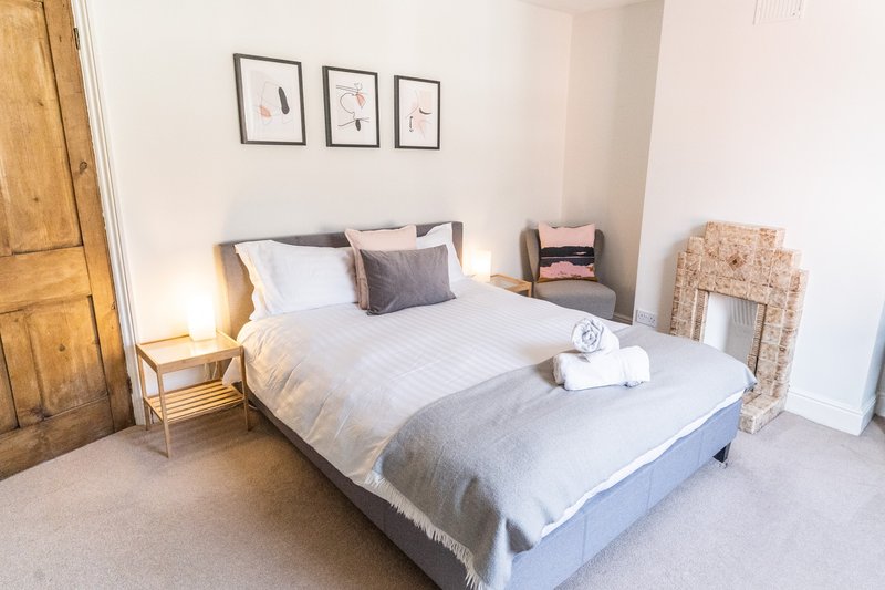 Bright bedroom with double bed, wooden door, bedside table, wall art and rolled towels