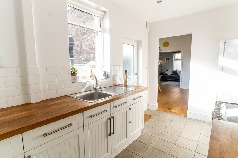 Bright kitchen with white cabinetry, wooden countertop, sink and window overlooking street