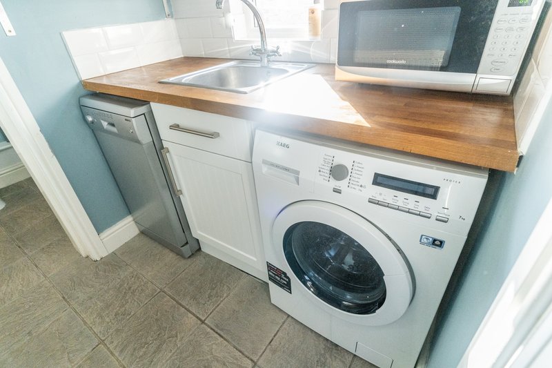 Compact kitchen with washing machine, sink, microwave and wooden countertop