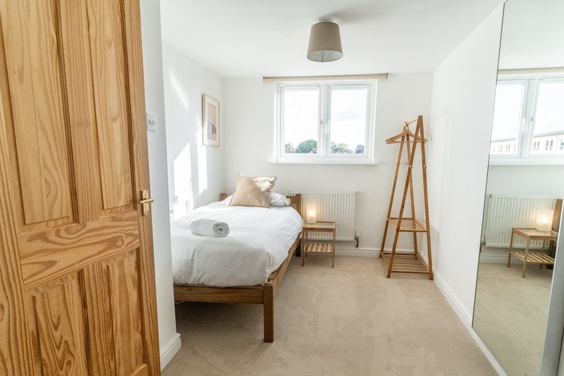 Bright bedroom with single bed, wooden wardrobe, mirror, and window with countryside view