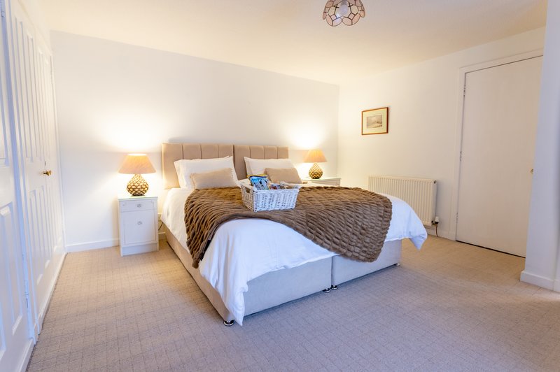 Bright bedroom with double bed, neutral bedding, twin lamps, and cream carpet flooring