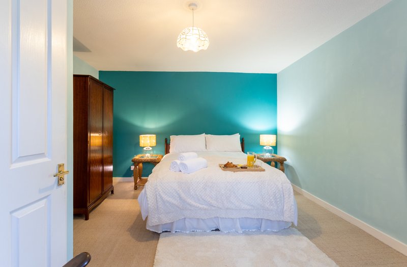 Bedroom with teal accent wall, double bed, wooden wardrobe and bedside lamps