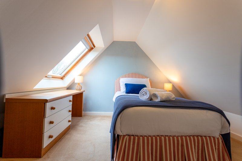 Attic bedroom with sloped ceiling, single bed, wooden dresser and skylight window