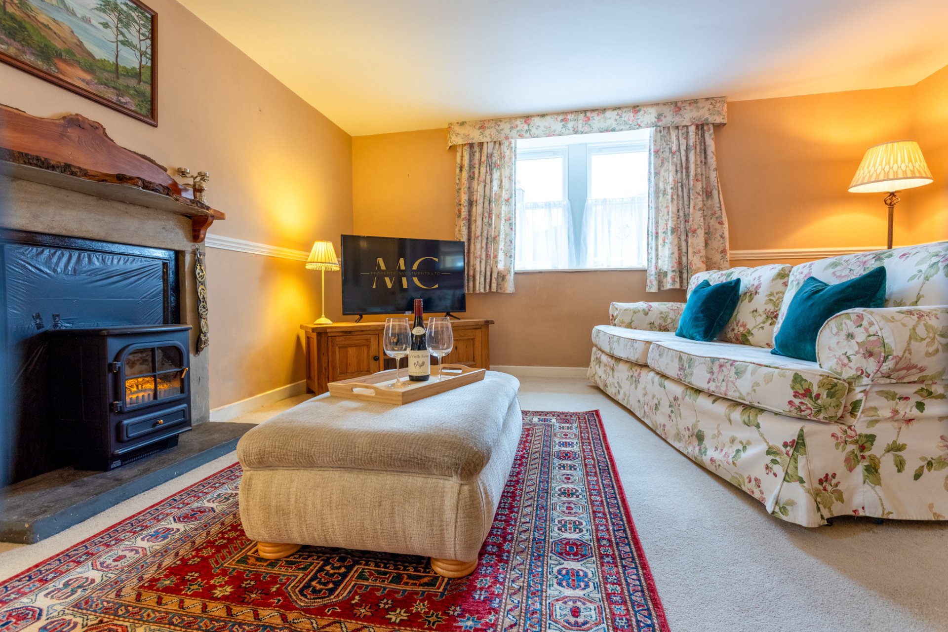 Warm living room with fireplace, patterned sofa, ottoman, TV, and decorative artwork