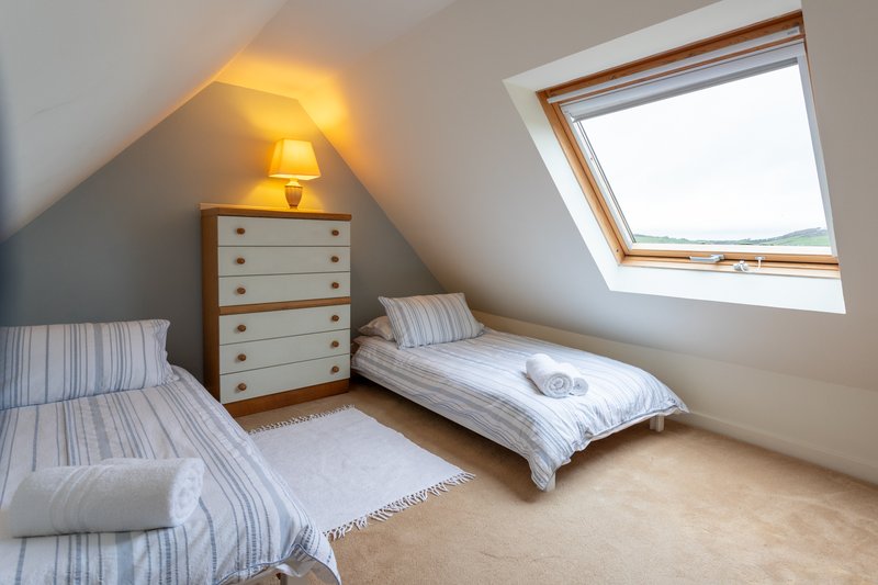 Bright attic bedroom with two single beds, wooden chest of drawers, and skylight window