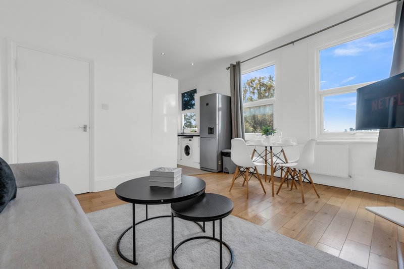 Modern living room with grey sofa, round black coffee table, dining chairs and kitchenette by window