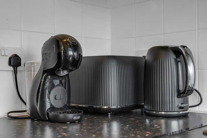 Kitchen counter with black coffee machine, kettle, and small appliances against white tiles